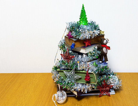 New Year celebration in the office. Stylized Christmas tree from old books decorated with Christmas toys on a wooden table. Free space for congratulatory text. Creative holiday background - Powered by Adobe