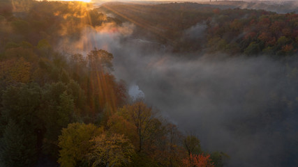 aerial perspective sunrise over a falls on river.  fog is seen over the river and the tree are in full bloom with autumn colors