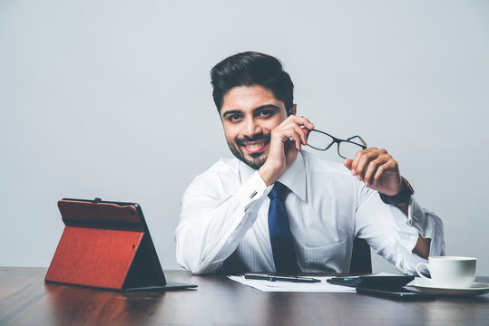 Bearded Indian Businessman accounting while sitting at desk / table in office