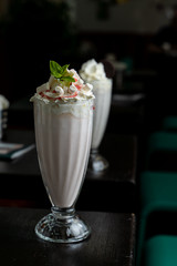 Two glasses of vanilla milkshake with whipped cream on dark wooden bar counter in a retro cafe