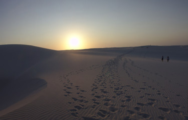 A group walks between the sand dunes of Lençois Maranhenses national Park lefting footprints behind