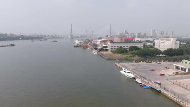 Flying drone along the port. Boats, tugboats, large cargo ships are moored in the frame. In the background a high bridge over the river and the city of Guangzhou, China
