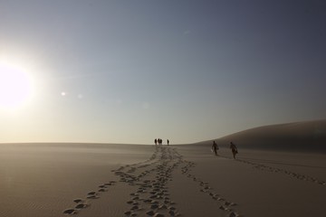 A group walks between the sand dunes of Lençois Maranhenses national Park lefting footprints behind