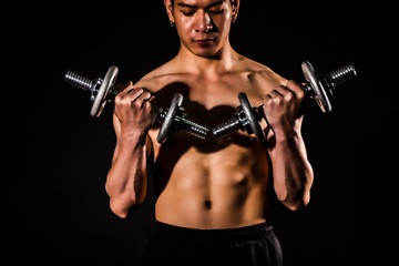 Naklejka na ściany i meble sport man standing doing exercise for arms with dumbbells and showing muscle bodybuilding on black backgrounds, fitness concept, sport concept
