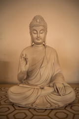 Buda de frente con mano levantada con pared blanca de fondo.