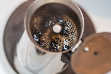 A cup of coffee maker is filled with fresh hot seething coffee with froth