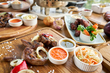 Lamb tongue kebab with Pickled cabbage and two sauces. Barbecue restaurant menu. Many different food on the table. Dinner party or Banquet
