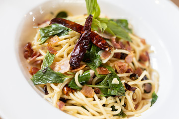 close up Stir-Fried Spaghetti With Dried Chili And Crispy Bacon in a White Plate.