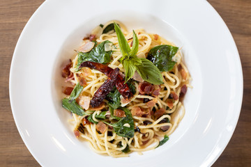 Top view of Stir-Fried Spaghetti With Dried Chili And Crispy Bacon in a White Plate on a wooden table.