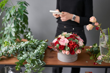 Floral shop concept . Woman florist read the cost of the bouquet on the calculator. arrangement in a round box. Handsome fresh bunch. Flowers delivery