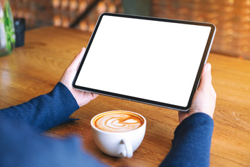 Mockup image of a woman holding black tablet pc with blank white screen with coffee cup on wooden table