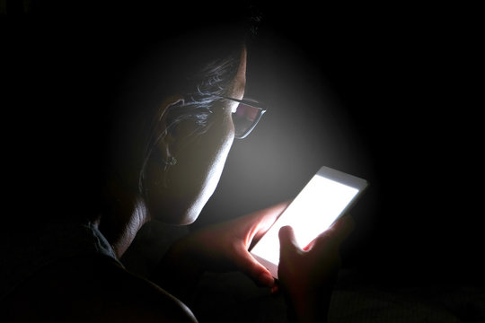 woman does not sleep and is stressed at night. She uses and looks smartphone in the bedroom without light and darkness.