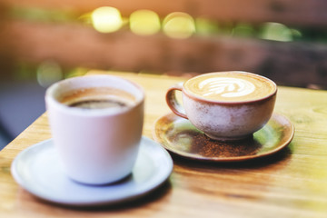 Closeup image of two cups of hot latte coffee and Americano coffee on wooden table