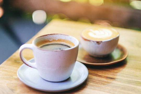 Closeup image of two cups of hot latte coffee and Americano coffee on wooden table