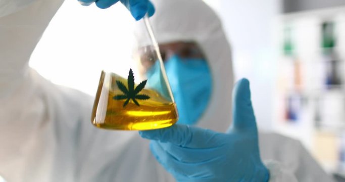 Male chemist mixing yellow liquid sbd oil closeup