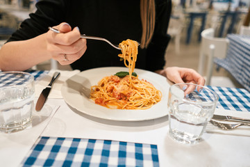 Close-up spaghetti Bolognese wind it around a fork. Parmesan cheese. Young woman eats Italian pasta...