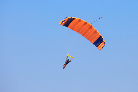 Skydiver under an orange parachute in blue sky