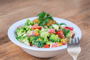 Delicious salad with broccoli, tomato, onion and boiled egg with cream sauce in plate on wooden background. Healthy food