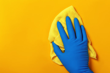 A hand in a protective latex glove holds a rag on a yellow colored background