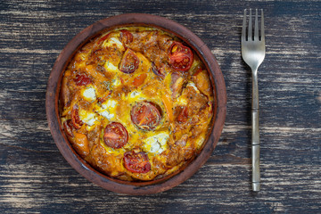 Ceramic bowl with vegetable frittata, simple vegetarian food. Frittata with tomato, pepper, onion and feta cheese on wooden table, close up. Italian egg omelette