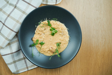 Traditional risotto with porcini mushrooms, cheese and microgreen in stylish black bowl on wooden background. Close up, selective focus. Italian cuisine