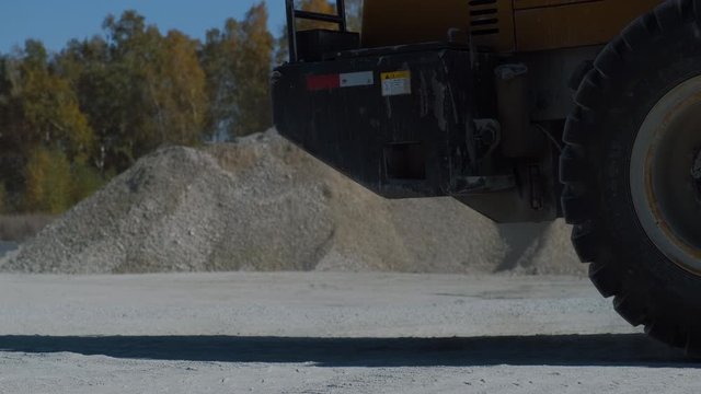 Close-up huge wheels of a mining truck. A huge loader is carrying gravel.