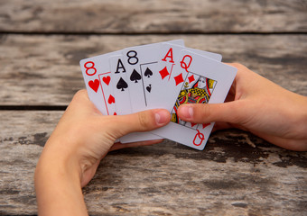 Playing cards in human hands on a wooden background.