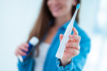 Happy smiling woman with ultrasonic electric toothbrush and toothpaste in bathroom at home. Dental hygiene and oral care, healthy teeth