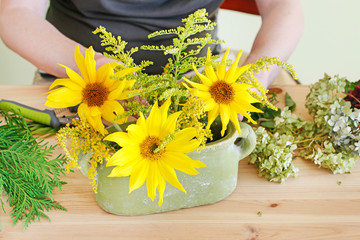 Woman shows how to make floral arrangement with sunflowers and hydrangeas