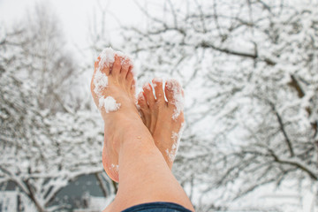 female bare feet, toes in the snow on a frosty winter day against a garden, hardening the body