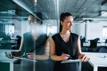 Young businesswoman with clipboard in an office, standing.