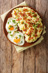 Rustic food mashed potato with bacon and parsley served with fried eggs closeup on a plate. Vertical top view