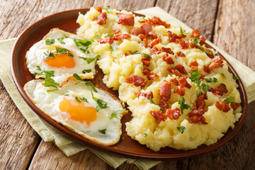 Tasty hot mashed potato with bacon and parsley served with fried eggs close-up on a plate. horizontal