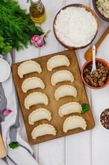 Uncooked vareniki (dumplings) on cutting wooden board on white background. Process of making vareniki with potatoes and fried mushrooms.  Traditional Russian and Ukrainian dish.