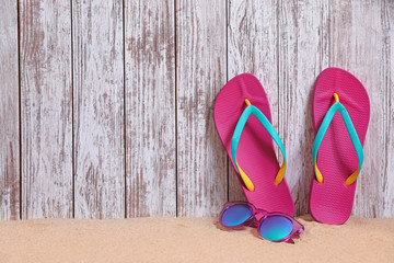 Bright flip flops and sunglasses on sand near wooden wall, space for text. Summer beach accessories