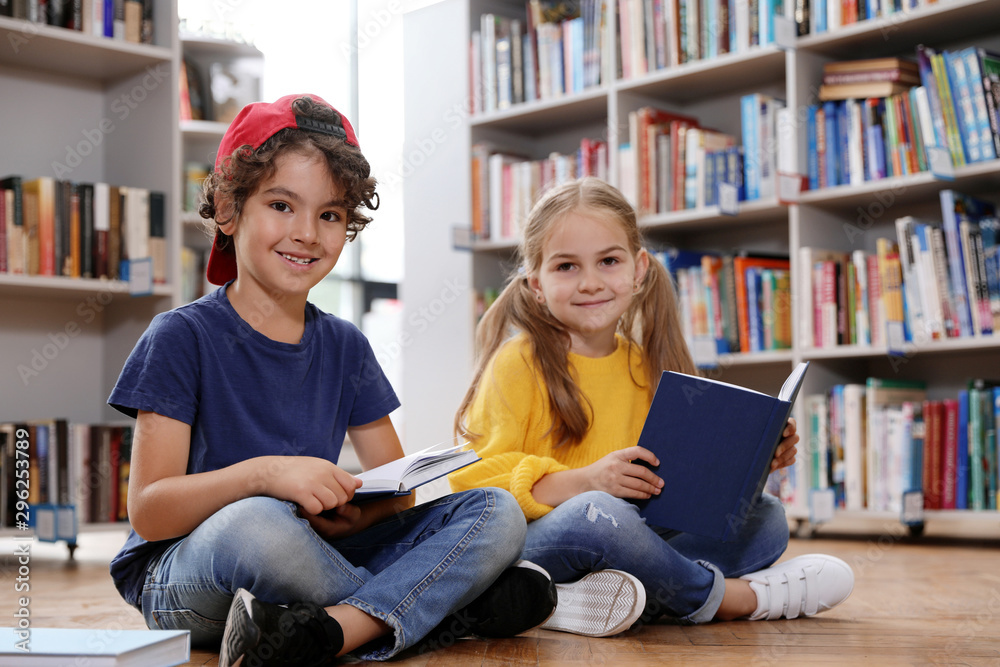 Wall mural Cute little children reading books on floor in library