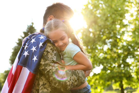 Father in military uniform with American flag holding his little daughter at green park