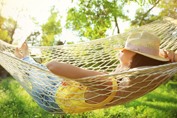 Young woman with hat resting in comfortable hammock at green garden