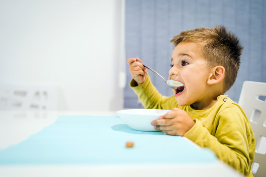 Portrait of small boy child eating soup meal or breakfast having lunch by the table at home with spoon white