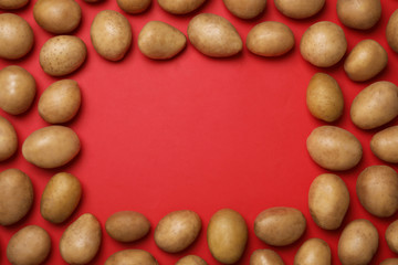 Frame made of raw fresh organic potatoes on red background, flat lay. Space for text