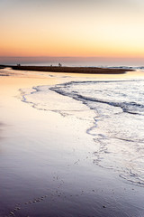 Groups of walkers create silhouettes that stand out in the sunset light on a beach in the Atlantic Ocean at Cap Ferret in France