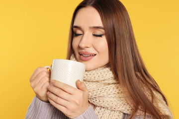 Beautiful young woman in sweater with drink on yellow background. Winter season