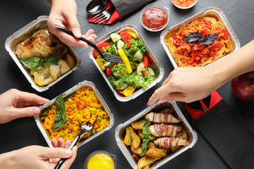 People eating from lunchboxes at grey table, top view. Healthy food delivery