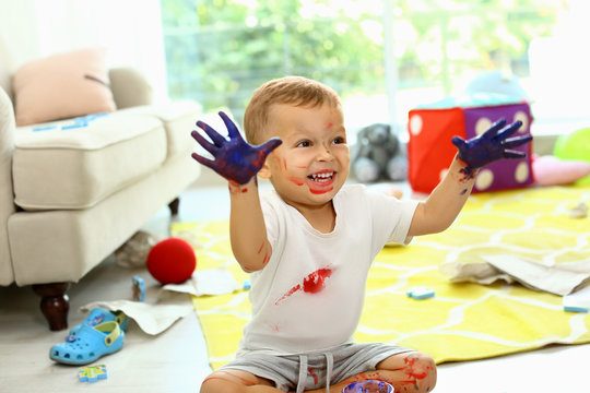 Cute little boy playing with paints on floor in living room