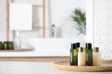 Wooden tray with mini bottles of cosmetic products on white table in bathroom. Space for text