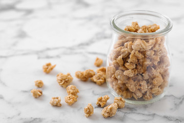 Jar with healthy granola on white marble table. Space for text