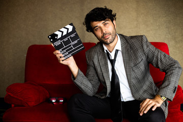 Portrait of film director man with clapboard sitting on red sofa