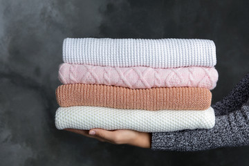 Woman holding stack of warm clothes on dark background, closeup. Autumn season