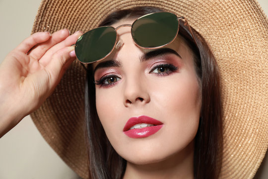 Beautiful woman with stylish sunglasses and hat on beige background