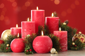 Fototapeta na wymiar Burning candles and Christmas decor on table against red background with bokeh effect